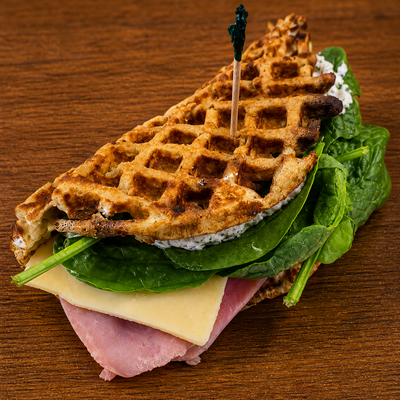 Waffle sandwich with ham, cheese, and spinach on a wooden surface