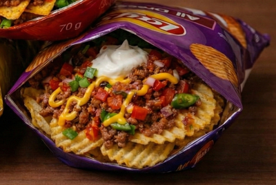 Three open bags of loaded nachos with various toppings on a wooden surface.